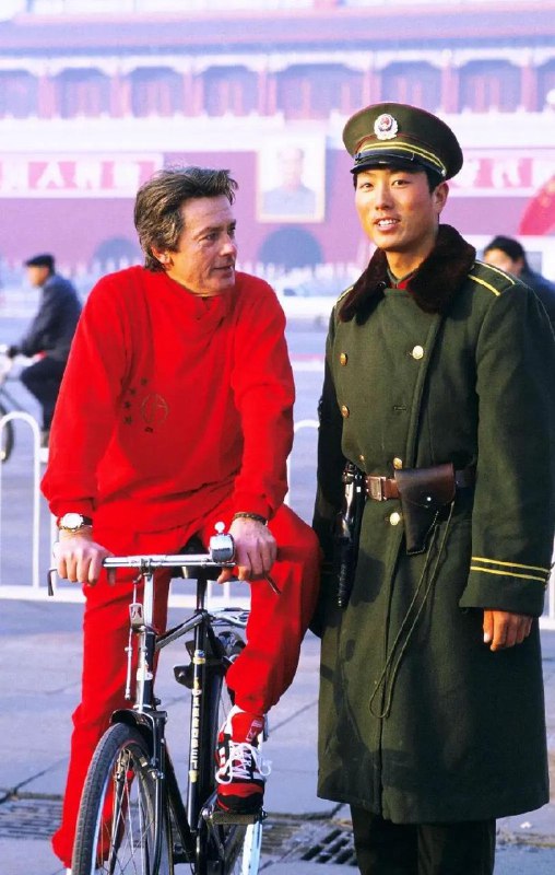 【老照片】1987年 ，已五十二岁的法国影星阿兰 •德隆在北京旅游时的留影，身穿红色运动服的他，骑着凤凰牌自行车逗留在天安门广场